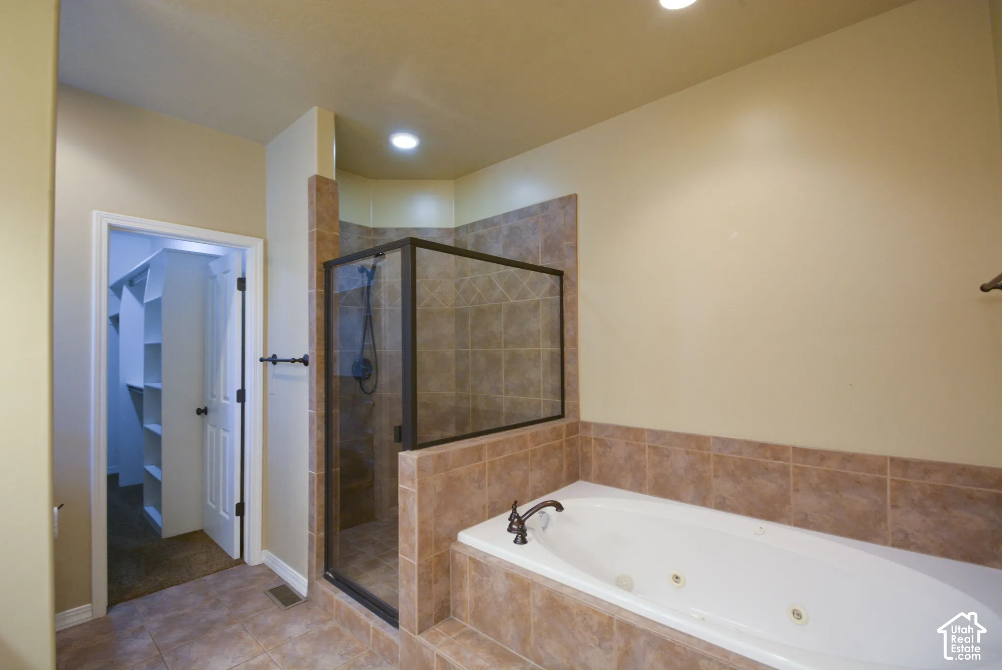 Tiled flooring and bath surround, enclosed shower with a dark-framed door, built-in jetted tub, and recessed lighting