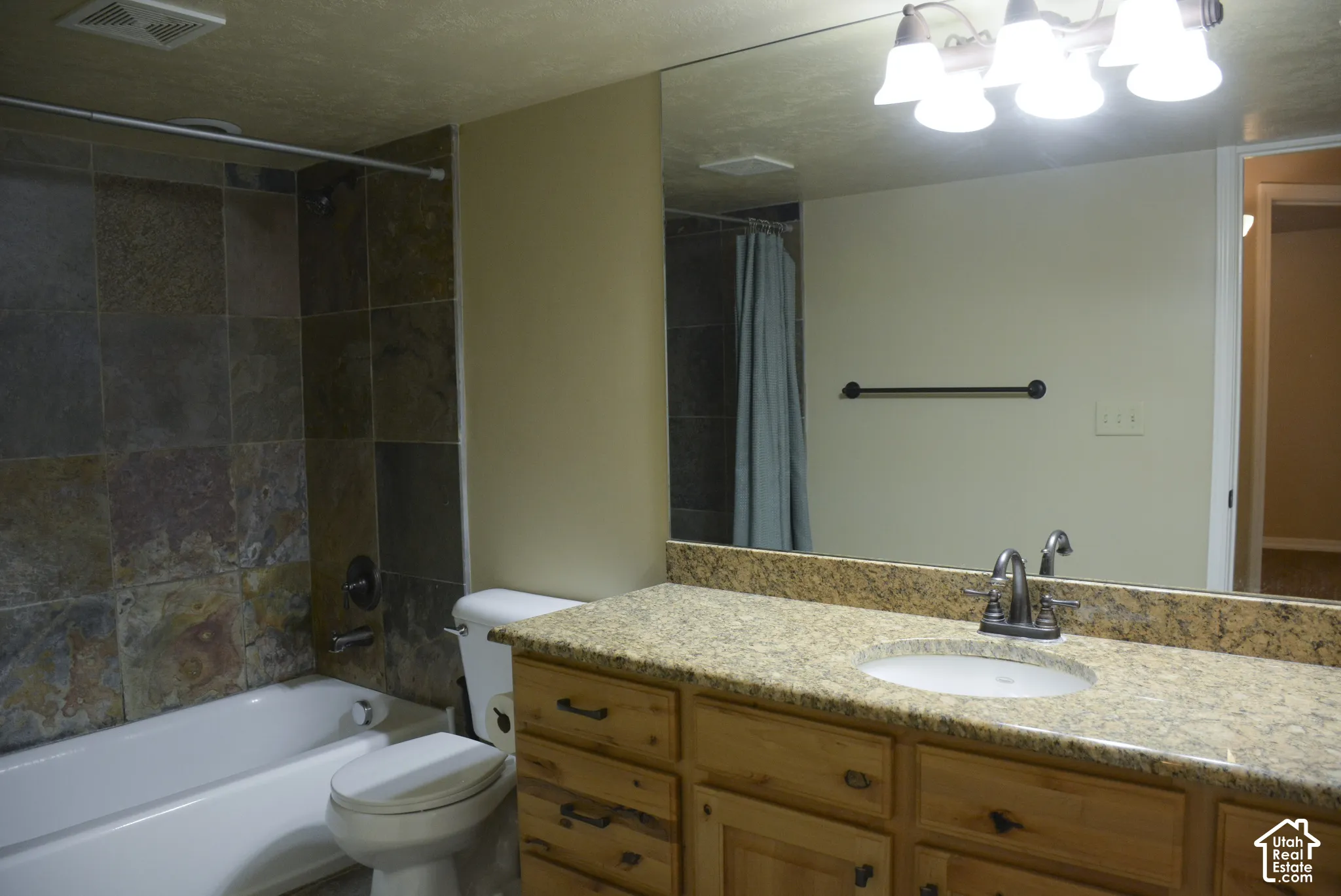 Bathroom featuring a ceramic bathtub, stone-tile shower surround, a vanity with wood-finish cabinetry, a large mirror, and a built-in light fixture