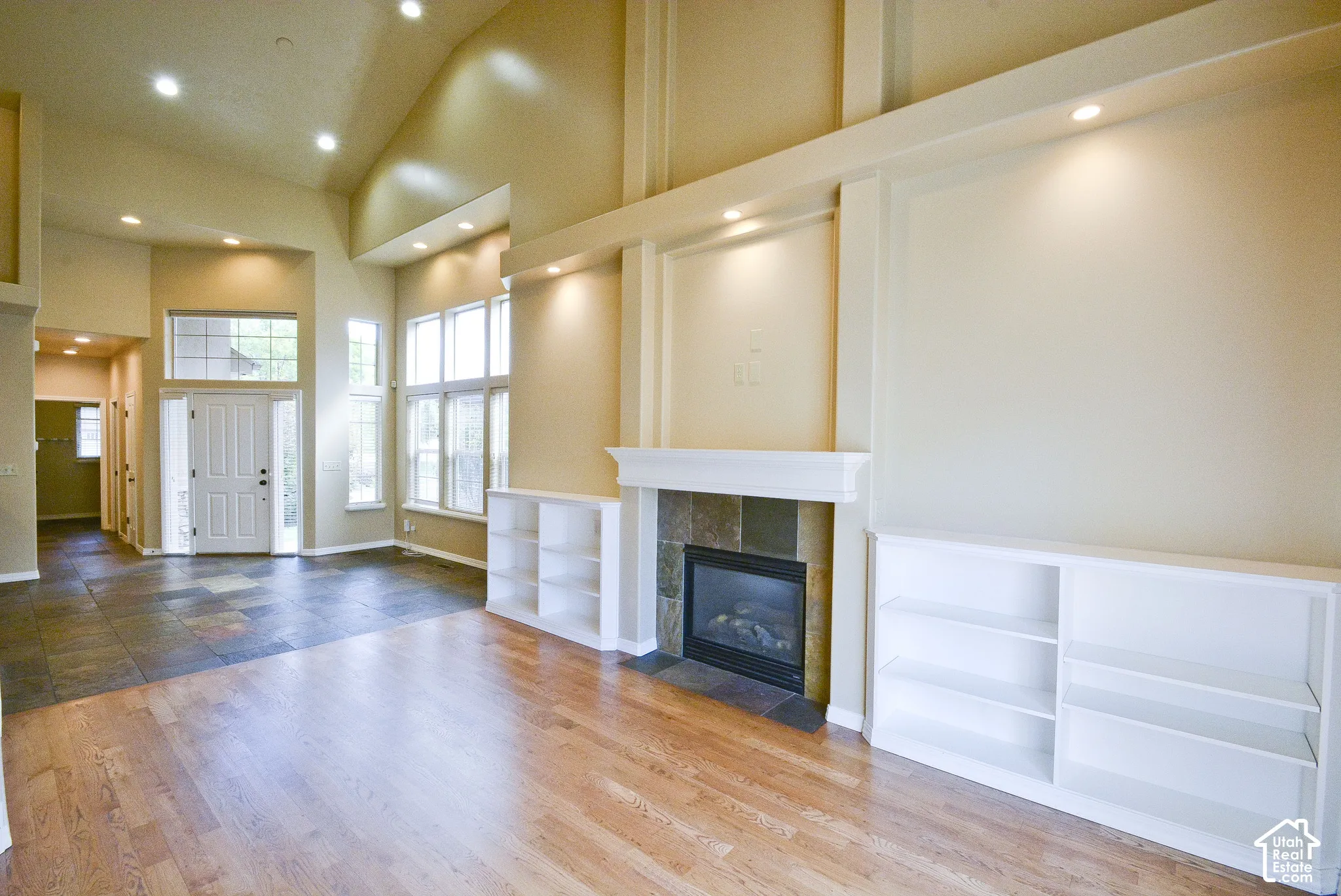 Vaulted ceiling with recessed lighting, combined hardwood and tile flooring, and a fireplace with a stone surround and built-in shelving