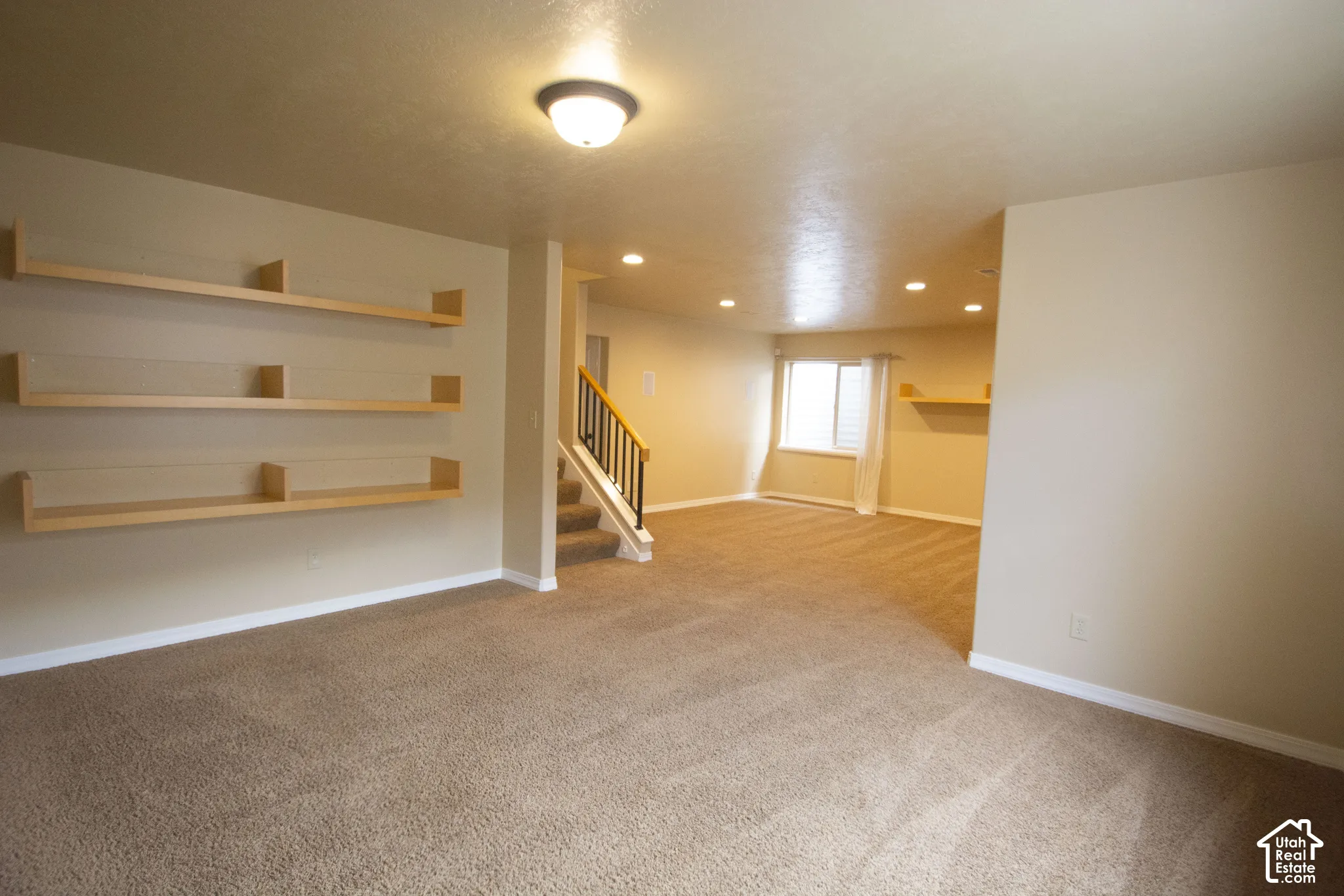 Soft carpet flooring throughout, built-in shelving, staircase with wood banister, recessed ceiling lighting, and a window with blinds