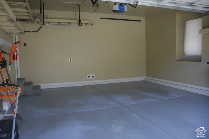Concrete flooring, neutral wall paint, overhead garage door mechanism, steps, and a window with blinds