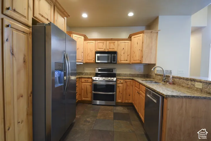 Kitchen featuring wood cabinetry, stainless steel appliances, granite countertops, and slate tile flooring