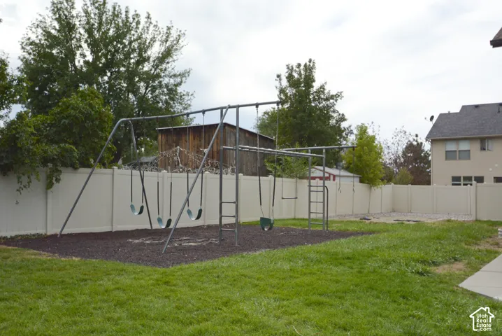 Expansive backyard featuring a manicured lawn, a swing set with a wood chip base, and a perimeter fence