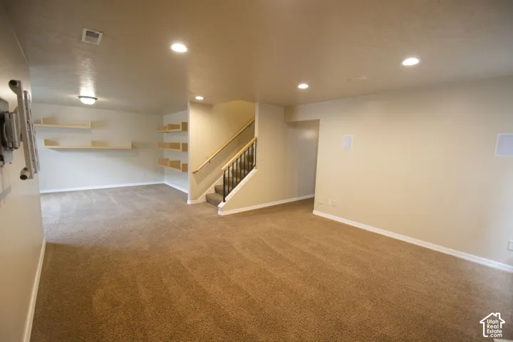 Spacious carpeted room featuring recessed lighting, built-in wall speakers, a staircase with a wooden handrail and wrought iron balusters, and integrated shelving