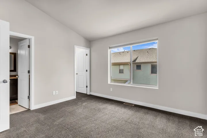 Primary suite with vaulted ceiling, neutral wall paint, gray carpeting, dual-pane window, and white trim