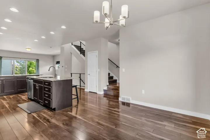Wood-finish flooring throughout, kitchen island with built-in sink and dishwasher, recessed lighting, contemporary chandelier, and a staircase with open risers and metal railings
