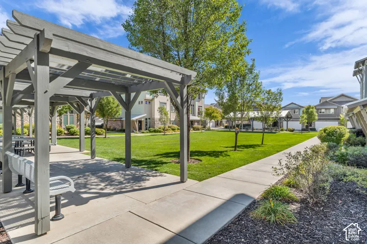Covered outdoor seating area with multiple benches, concrete walkway, and landscaped green space