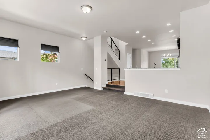 Carpeted main living area with neutral wall color, two windows with roller blinds, and flush-mount lighting fixtures