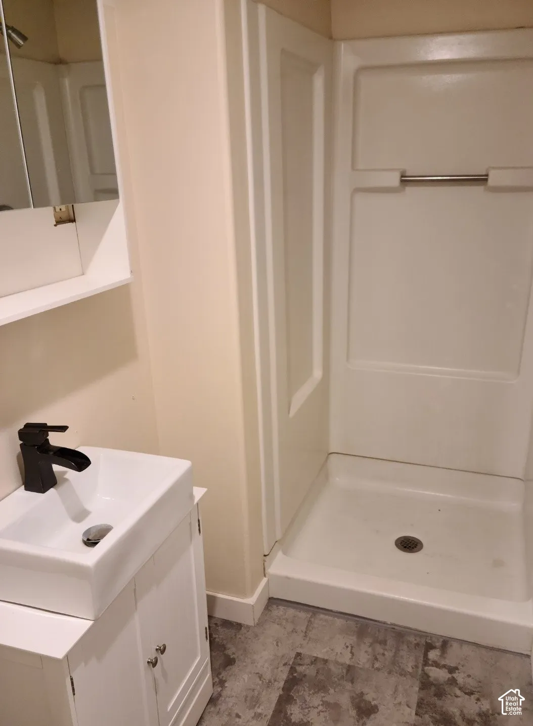 Compact bathroom featuring a white vanity with storage, rectangular vessel sink, matte black faucet, and a white shower stall with a built-in shelf