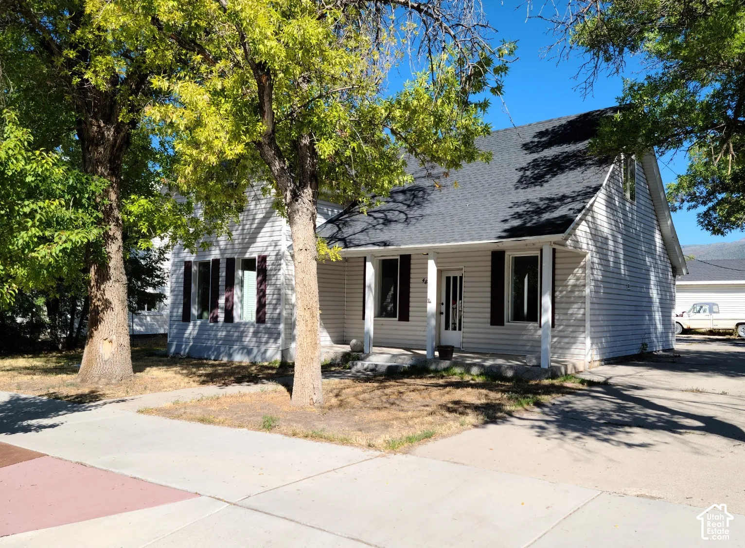 Gabled roofline with asphalt shingles, white siding exterior, covered front porch, and black window shutters