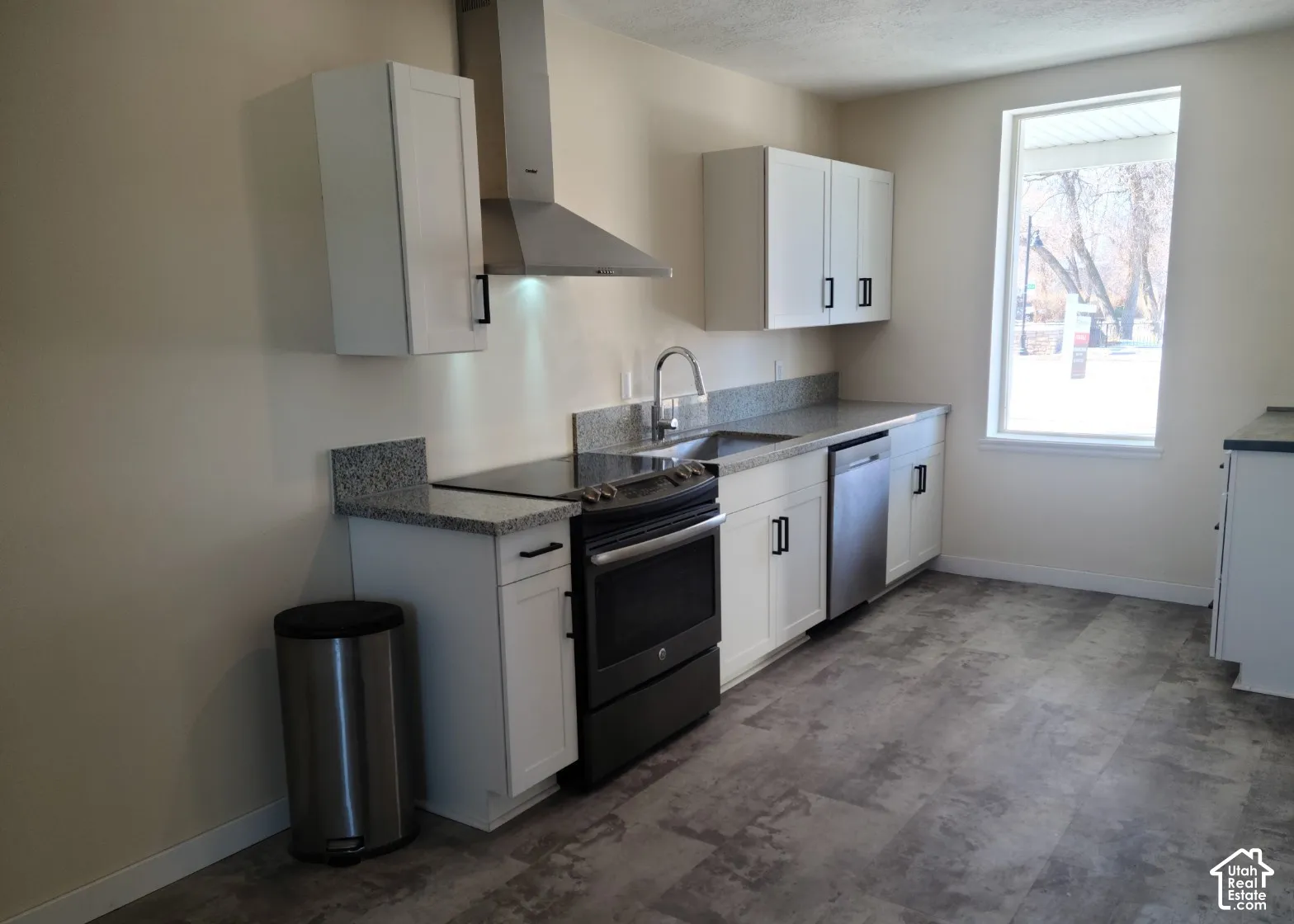 White cabinetry with matte black hardware, stainless steel appliances, granite-finish countertops, stainless steel sink, and wood-finish flooring