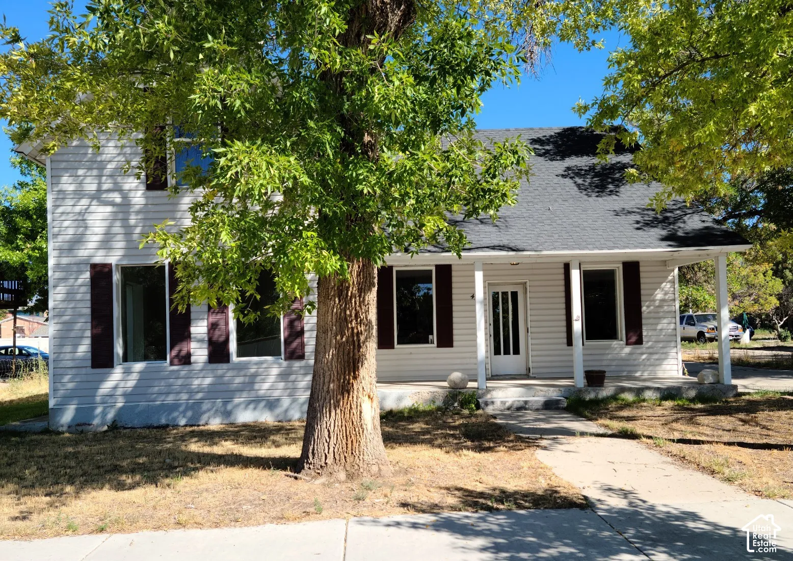Two-story exterior with white siding, dark shutters, covered front porch, and mature trees