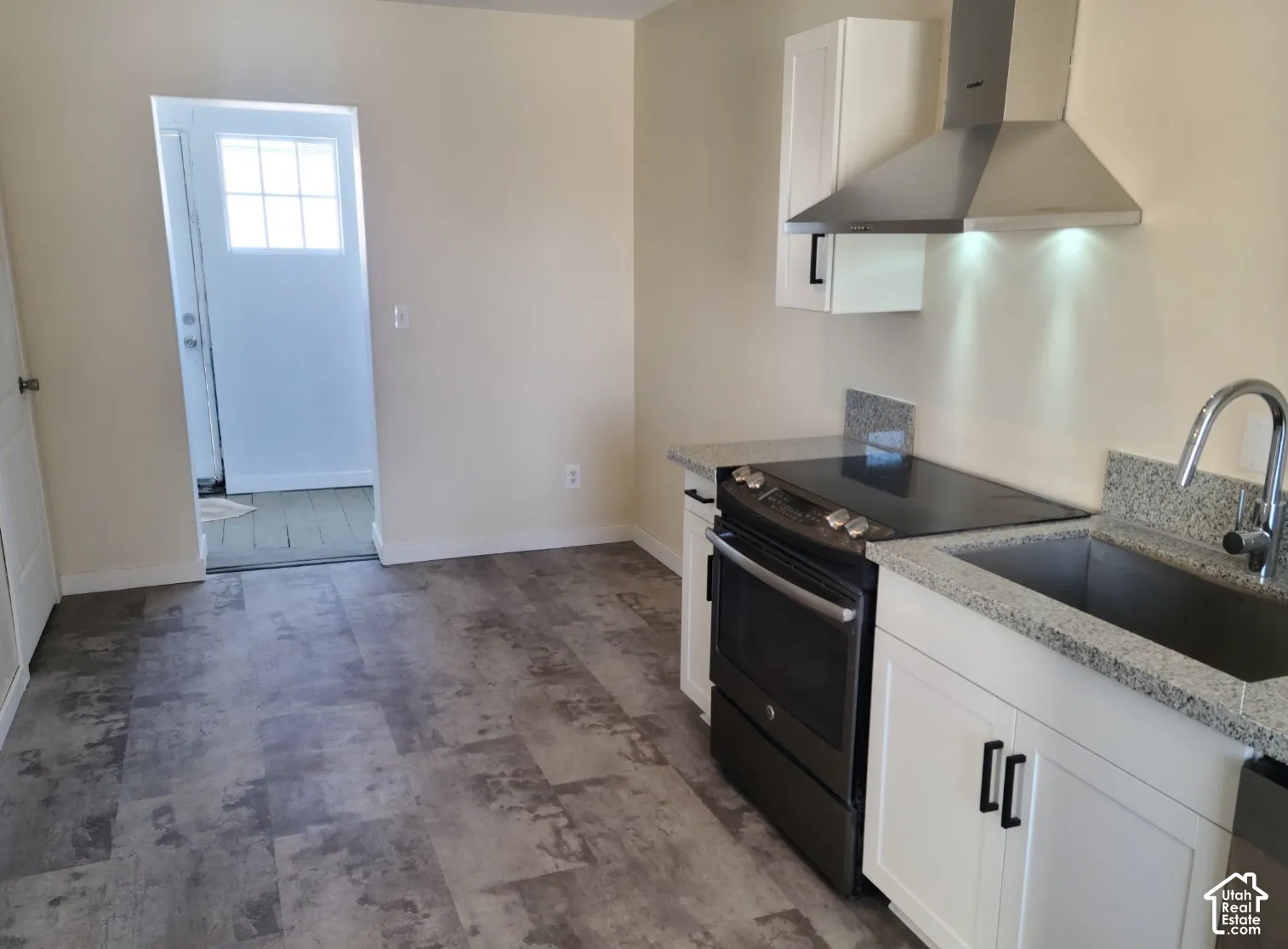 White cabinetry with dark hardware, stone countertops, stainless steel sink with gooseneck faucet, black range, and stainless steel range hood