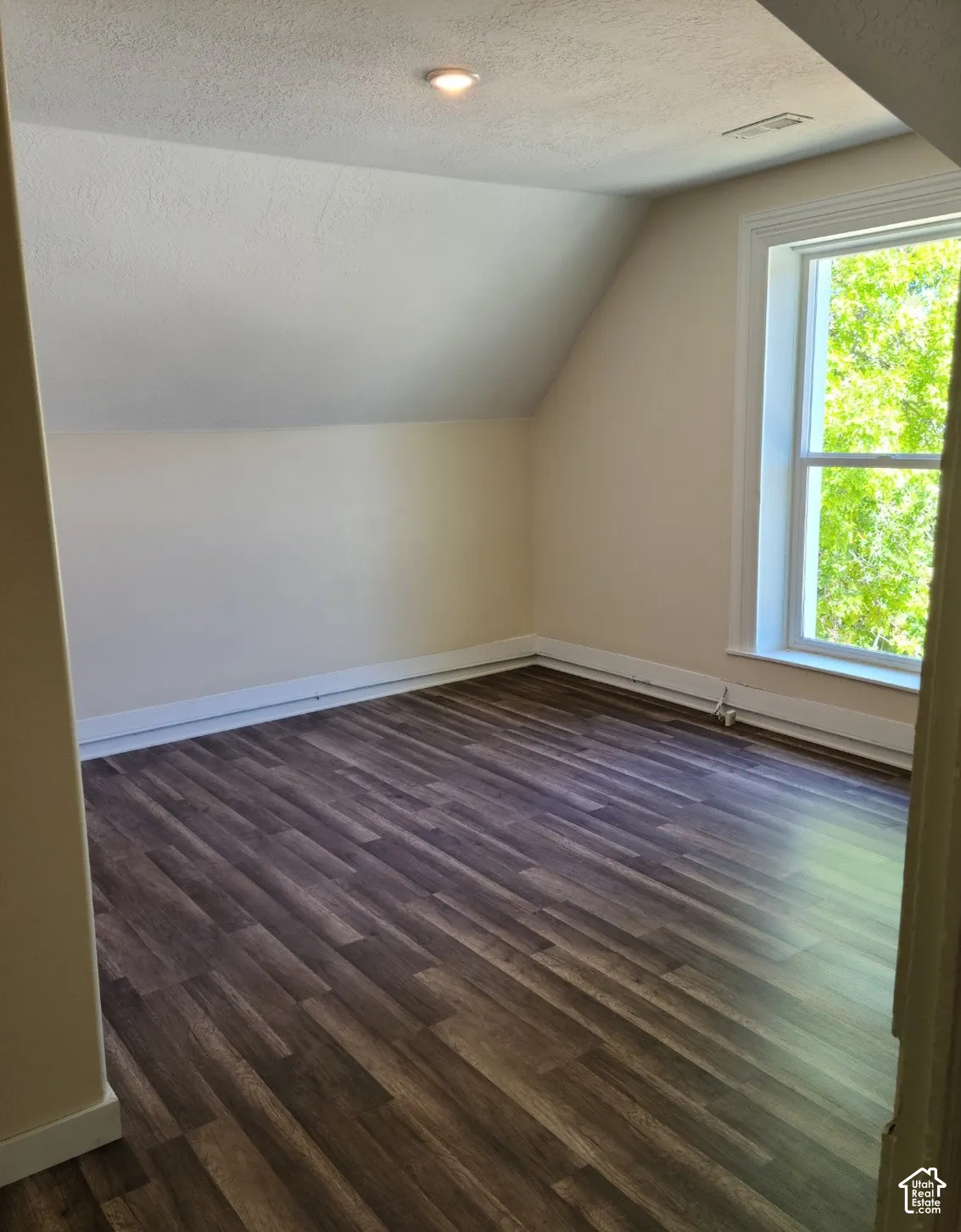 Angled ceiling with a recessed light fixture, a large window, and wood-finish flooring