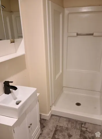Compact bathroom featuring a white vanity with storage, rectangular vessel sink, matte black faucet, and a white shower stall with a built-in shelf