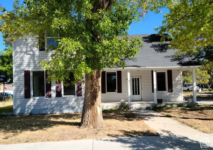 Two-story exterior with white siding, dark shutters, covered front porch, and mature trees
