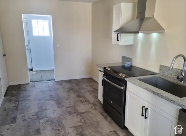 White cabinetry with dark hardware, stone countertops, stainless steel sink with gooseneck faucet, black range, and stainless steel range hood
