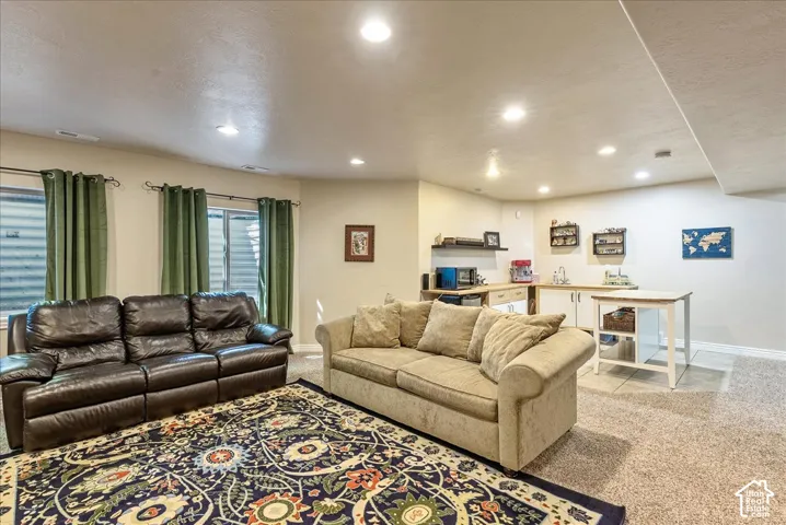 Recessed lighting, carpet flooring, multiple windows, built-in shelving, and a wet bar with a stainless steel sink