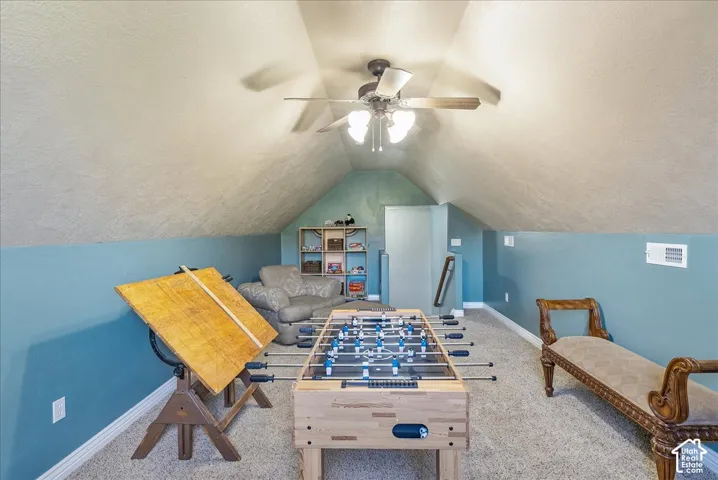 Carpeted attic space featuring sloped ceilings, a ceiling fan with integrated lighting, and a built-in wall niche