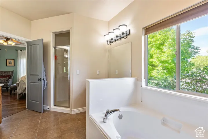 Built-in soaking tub, separate glass-enclosed shower, light-colored wall paint, tile flooring, and a large window