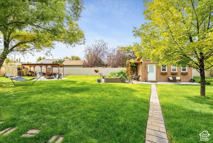 Expansive green lawn with mature trees, a paved pathway, a wooden pergola, a separate garden structure with a white door, and a privacy fence