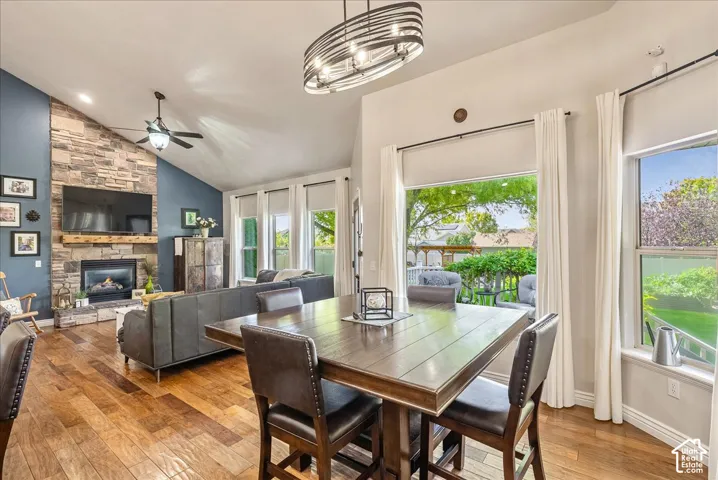 Vaulted ceilings, a stone-clad fireplace with a wood mantel, wood-finish flooring, and expansive windows providing outdoor visibility