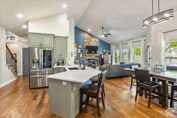 Vaulted ceilings, wood-finish flooring, stone fireplace, kitchen island with seating, and a built-in stainless steel refrigerator