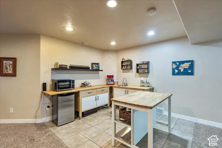 Wet bar featuring wood-finish countertops, tile flooring, built-in cabinetry, and a stainless steel sink