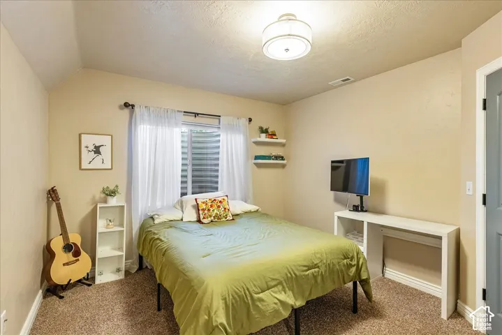 Carpeted flooring, vaulted ceiling, recessed window, ceiling-mounted light fixture, and a built-in desk with shelving