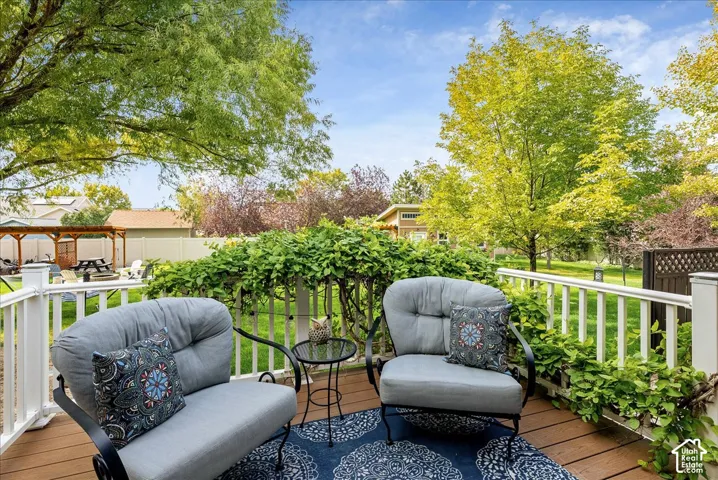Wood-finish deck with white railing, featuring extensive greenery and mature trees