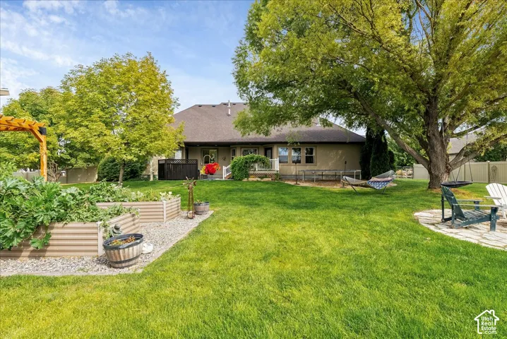 Expansive backyard featuring a manicured lawn, established shade trees, raised garden beds, and a paver patio