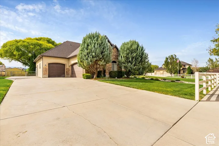 Stucco exterior with stone accents, a two-car garage, a concrete driveway, and a manicured front lawn