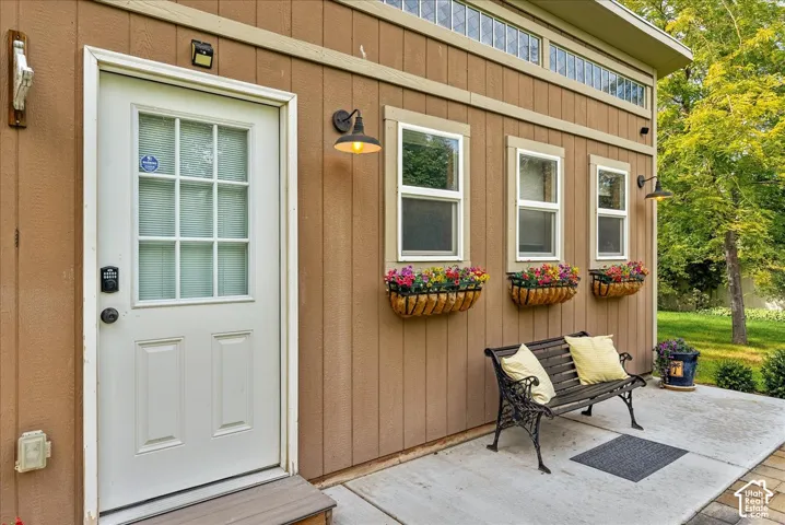 Board-and-batten siding with an entry door featuring a transom window, multiple windows, and a concrete patio