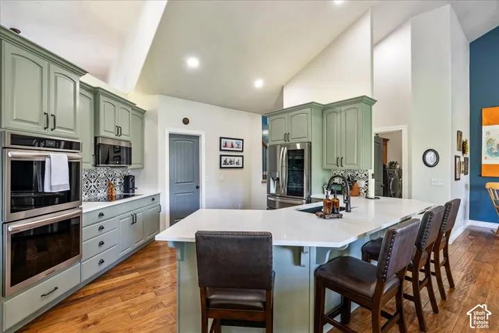 Kitchen featuring sage green cabinetry, stainless steel appliances, a white island with seating, and wood-finish flooring