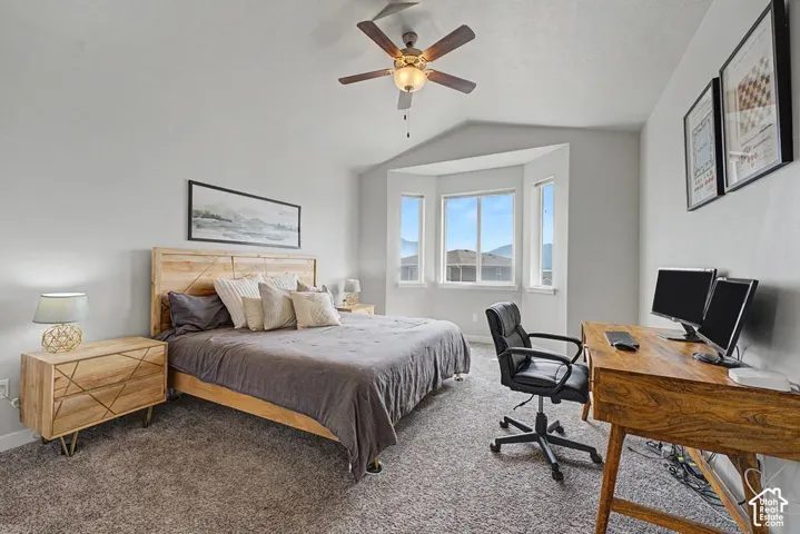 Angled ceiling with a ceiling fan, bay window, light grey walls, and grey carpeting