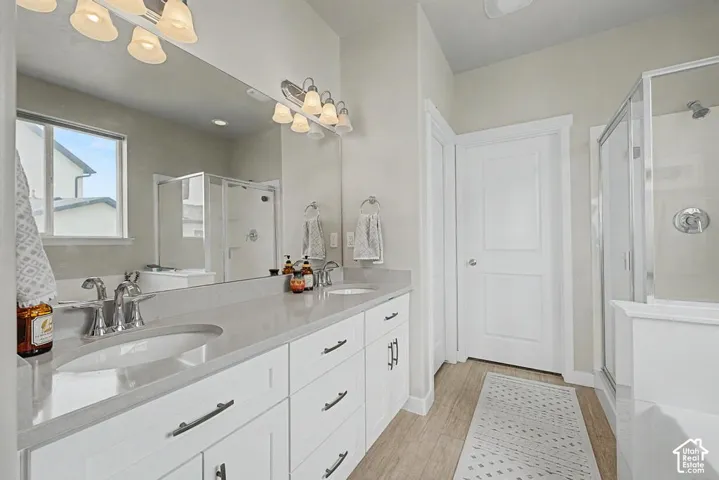 Dual vanity with undermount sinks, stone countertop, wood-finish flooring, and a glass-enclosed shower