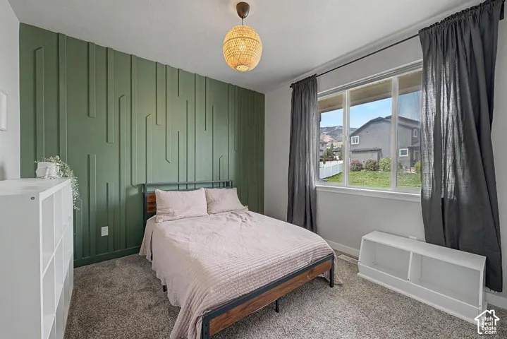 Accent wall with geometric paneling, carpeted flooring, and a large window with roller shades