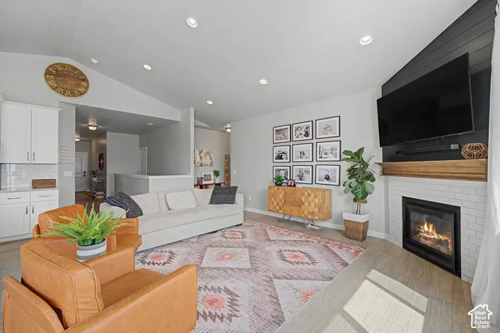 Vaulted ceilings, recessed lighting, wood-finish flooring, white subway tile fireplace surround, and a natural wood mantel