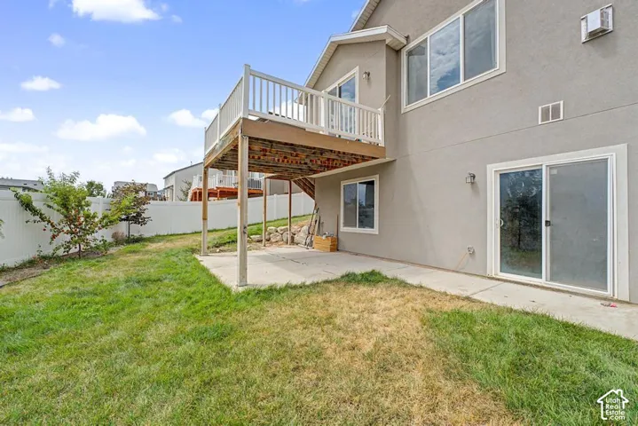 Rear exterior featuring a ground-level concrete patio, upper-level wood deck with white railing, and a sliding glass door