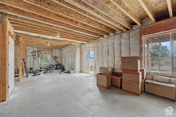 Unfinished basement space with exposed wood joists and concrete flooring, featuring a sliding glass door and an additional window