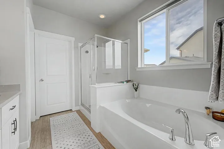 Soaking tub with deck-mounted chrome fixtures, glass-enclosed shower, and wood-finish flooring