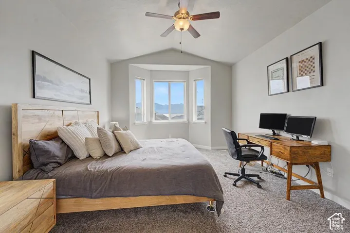 Vaulted ceiling with a ceiling fan, bay window with multiple panes, light gray wall paint, and gray carpet flooring