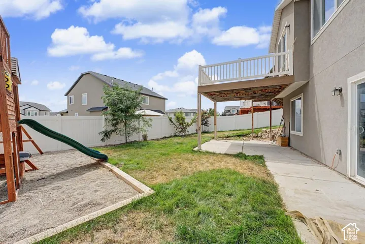 Expansive backyard featuring a concrete patio, elevated deck with white railing, and perimeter fencing