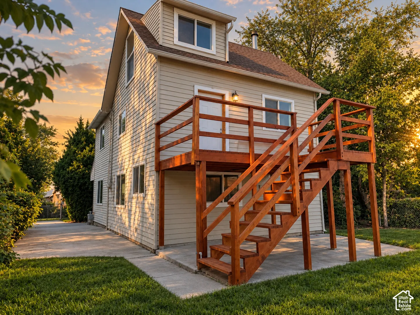 Multi-story residence featuring light-colored siding, a second-story wooden deck with stairs, a concrete patio, and a manicured lawn
