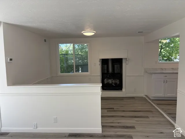Wood-finish flooring, white paneled walls, a built-in stove, a window with outdoor scenery, and white cabinetry with a light-colored countertop