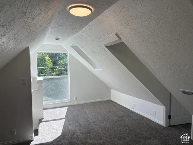 Carpeted room with sloped ceilings, recessed wall alcoves, and a large window