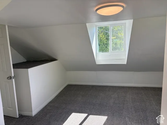 Carpeted room featuring an angled ceiling, built-in storage, a ceiling-mounted light fixture, and a framed window