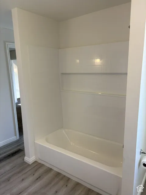 Bathtub with a tiled surround, integrated shower niche, and wood-finish flooring