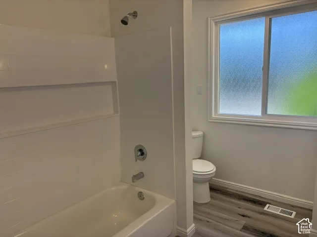 White tub and shower combination with a built-in niche, chrome fixtures, and wood-finish flooring