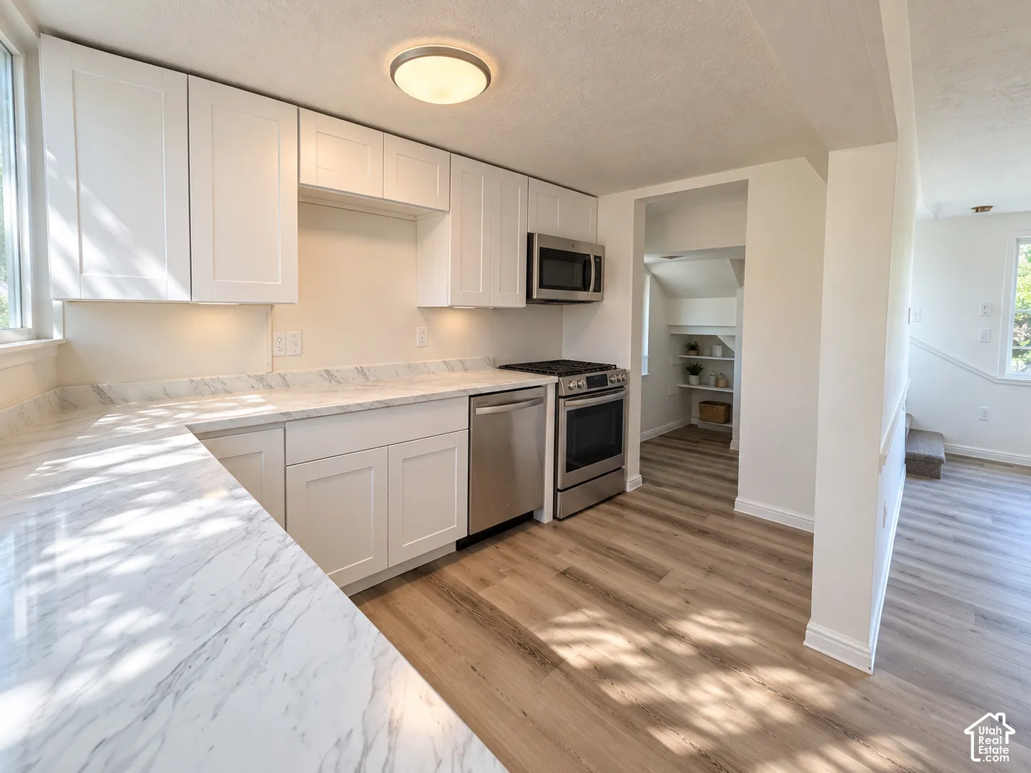 White cabinetry, stainless steel appliances, light-toned countertops, wood-finish flooring, and recessed lighting